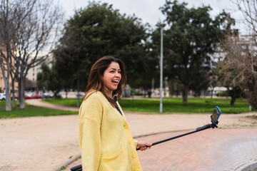 Young woman vlogger recording video for social media with selfie stick in a park