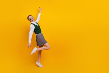 Joyful teenager posing against yellow background wearing a stylish uniform and expressing happiness...