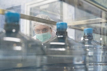 Drinking water manufacturers. Water filling machine. 20 Liter bottled on conveyor during filling water drinking from water filling machine. Female worker working in production line