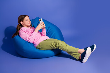 Smiling young girl in casual attire using a smartphone while relaxing on a blue beanbag with a vibrant background