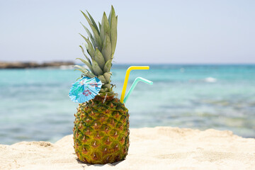 Ripe pineapples  cocktail with straw and umbrella on the sandy tropical beach background with copy space. Leisure in summer and Summer vacation concept