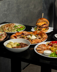 Table scene with a variety of delicious foods. Angled and perspective View over a dark wood background.