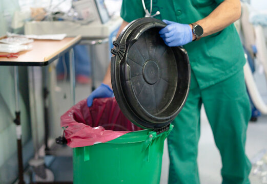 Doctor wearing green scrubs opening biohazard medical waste container in hospital room