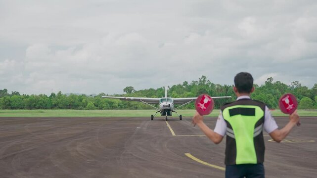 A small turboprop plane lands at a remote airport. A marshal guides the pilot to a parking spot