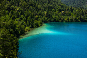 turquoise lake with rich, bright clear water surrounded by lush green forested hills. pristine wilderness concept with copy space