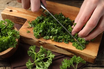 Woman cutting parsley at wooden table, closeup