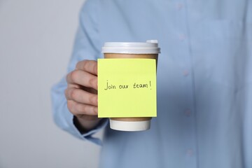 Join Our Team. Woman holding takeaway cup with sticky note on grey background, closeup