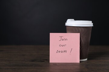 Paper note with phrase Join Our Team and cup of coffee on wooden table. Space for text