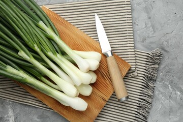 Fresh ripe green onions with cutting board and knife on grey textured table, flat lay