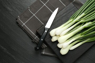 Fresh ripe green onions with cutting board and knife on black table, flat lay