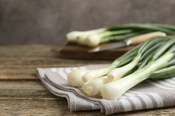 Fresh ripe green onions and towel on wooden table, closeup. Space for text