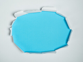 Tear hole in center of white paper reveals light blue background.