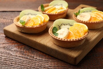 Tartlets with fruits and mint on wooden table, closeup. Delicious dessert