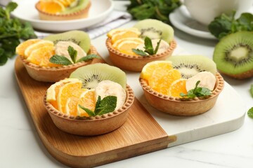 Tartlets with fruits and mint on white table, closeup. Delicious dessert
