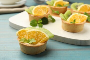 Tartlets with fruits and mint on light blue wooden table, closeup. Delicious dessert