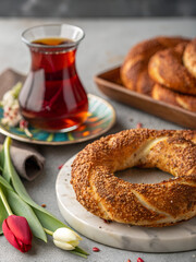 Turkish tea in a glass and a sesame simit with tulips on a table