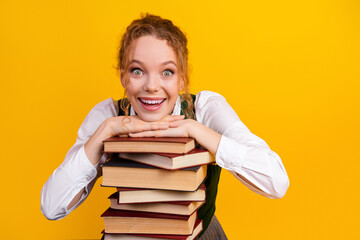Excited female student with stacked books against yellow background, showcasing youthful energy and...