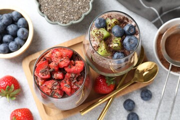 Delicious chocolate puddings with chia seeds and berries in glasses on grey table, flat lay