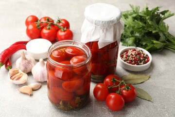 Tasty pickled tomatoes in jars and ingredients on light grey table, closeup