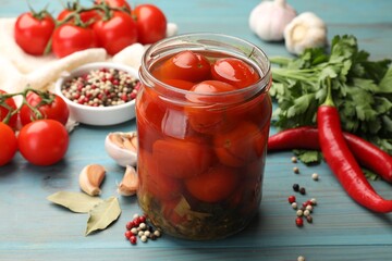 Tasty pickled tomatoes in jar and ingredients on light blue wooden table, closeup