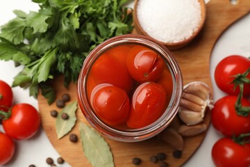 Tasty pickled tomatoes in jar and ingredients on white table, flat lay