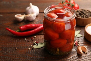 Tasty pickled tomatoes in jar and ingredients on wooden table, closeup