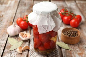 Tasty pickled tomatoes in jar and ingredients on wooden table, closeup