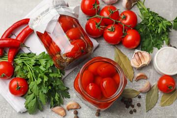Tasty pickled tomatoes in jars, products and spices on grey textured table, flat lay