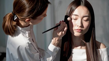 Woman eye makeup applied by beauty expert indoors with natural light. Concept of woman eye makeup highlights professional makeup techniques in soft, flattering lighting.