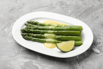 Tasty cooked asparagus served with sauce and lime on grey textured table