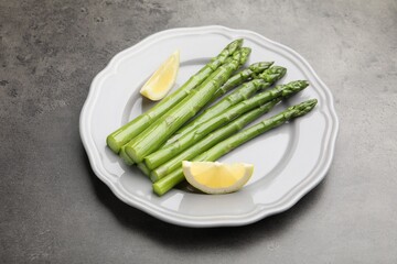 Tasty cooked asparagus served with lemon on grey table