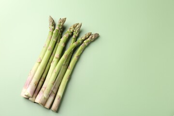 Fresh ripe raw asparagus on green background, flat lay. Space for text