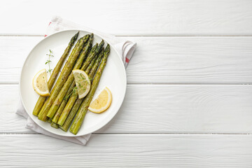 Tasty cooked asparagus served with lemon and thyme on white wooden table, top view. Space for text