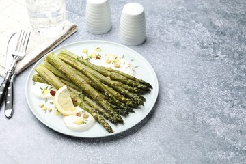 Tasty cooked asparagus served with lemon and sauce on grey table, space for text