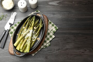 Tasty cooked asparagus served with parmesan on black wooden table, flat lay. Space for text