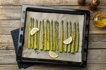 Tasty cooked asparagus and lemon on baking tray on wooden table, top view