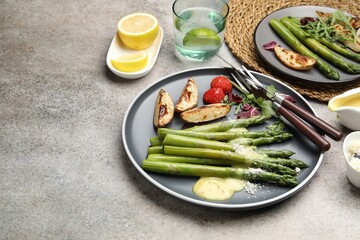 Tasty cooked asparagus served with baked potatoes, tomatoes and sauce on grey table, space for text