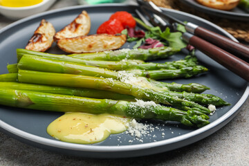 Tasty cooked asparagus served with baked potatoes, tomatoes and sauce on grey table, closeup