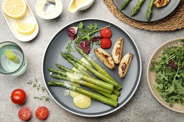 Tasty cooked asparagus served with baked potatoes, tomatoes and sauce on grey table, flat lay