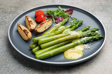 Tasty cooked asparagus served with baked potatoes, tomatoes and sauce on grey table, closeup