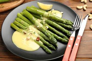 Tasty cooked asparagus served with lemon and sauce on wooden table, closeup