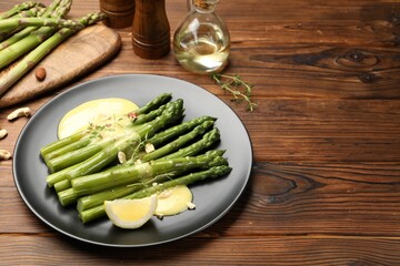 Tasty cooked asparagus served with lemon and sauce on wooden table, space for text