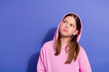 Portrait of a young girl wearing a pink hoodie looking thoughtful against purple background