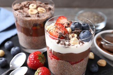Delicious chocolate puddings with chia seeds, nuts and berries in glasses on grey table, closeup