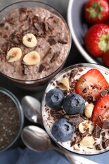 Delicious chocolate puddings with chia seeds, nuts and berries in glasses on grey table, flat lay