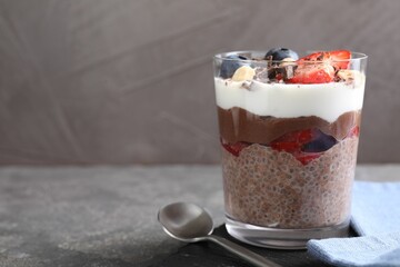 Delicious chocolate pudding with chia seeds, nuts and berries in glass on grey table, closeup. Space for text