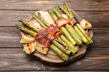 Tasty cooked asparagus served with bacon and potatoes on wooden table, closeup