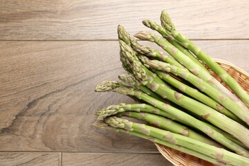 Fresh raw asparagus spears in wicker basket on wooden table, top view. Space for text