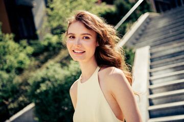 Young woman smiling outdoors on a sunny day while wearing a stylish yellow dress in an urban setting