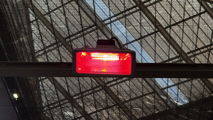 Red warning light aglow under an industrial lattice, akin to Diwali's flickering lamps or Kwanzaa's...